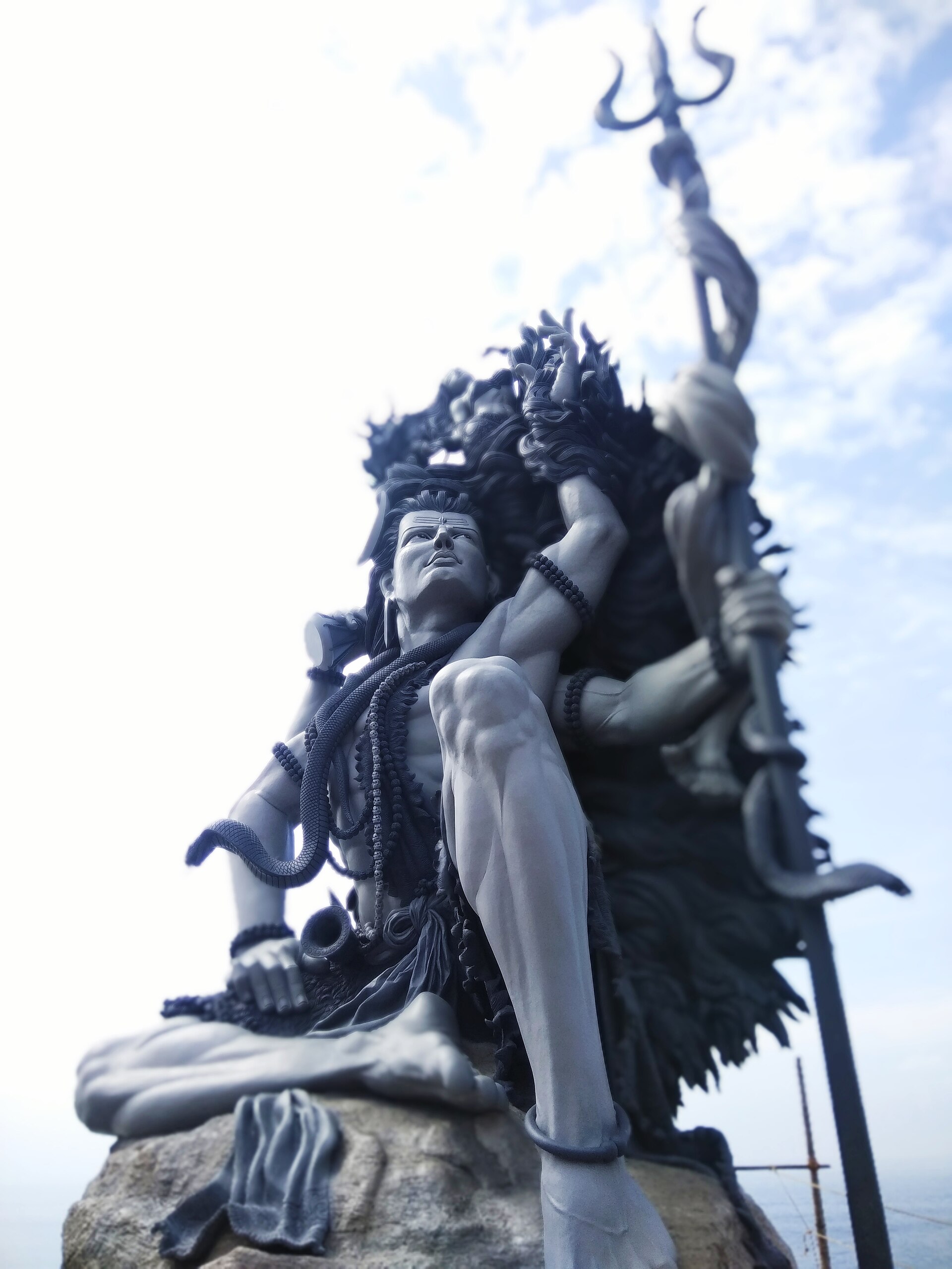 Low-angle view of the Azhimala Shiva sculpture, trishul raised against the clouds