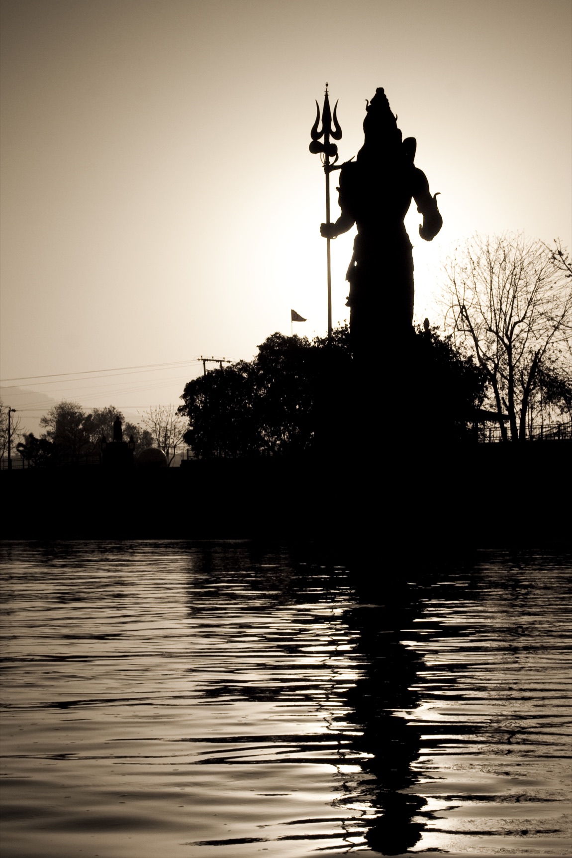 Silhouette of the tall Shiva statue with trishul at sunrise, reflected in the Ganga at Har Ki Pauri, Haridwar
