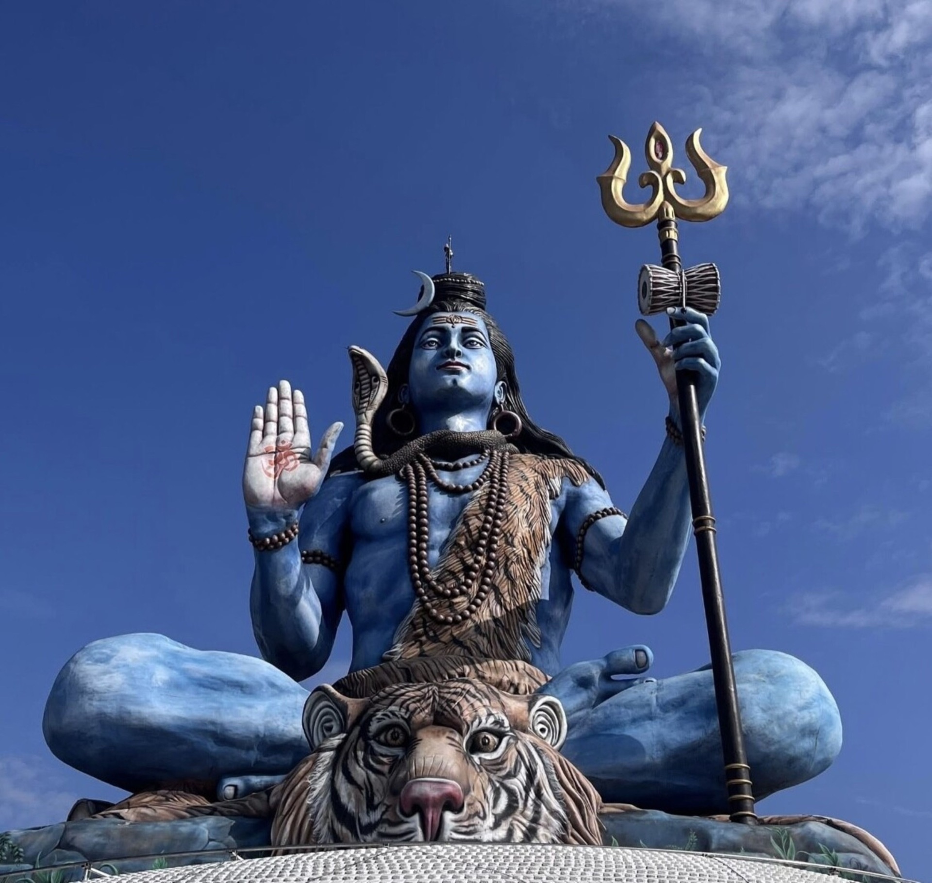 The blue Shiva statue of Pumdikot, Pokhara, seated on a tiger skin with a golden trishul against a deep blue sky